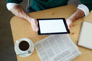 travailler avec des données, tablette tenue face a un journal, avec un café a coté